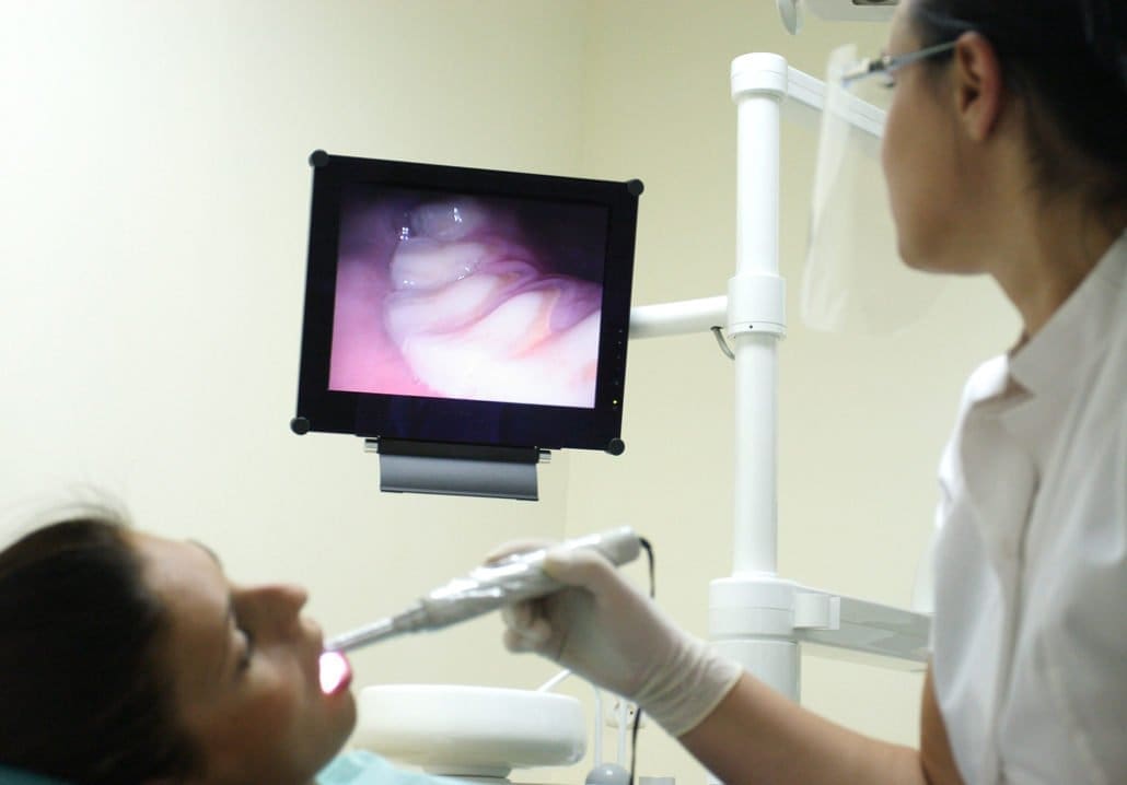 A dentist at Unique Dental of Framingham in Massachusetts examines a patient's oral condition on a medical monitor while inserting a camera into the patient's mouth.