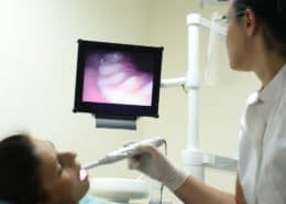A dentist at Unique Dental of Framingham in Massachusetts examines a patient's oral condition on a medical monitor while inserting a camera into the patient's mouth.